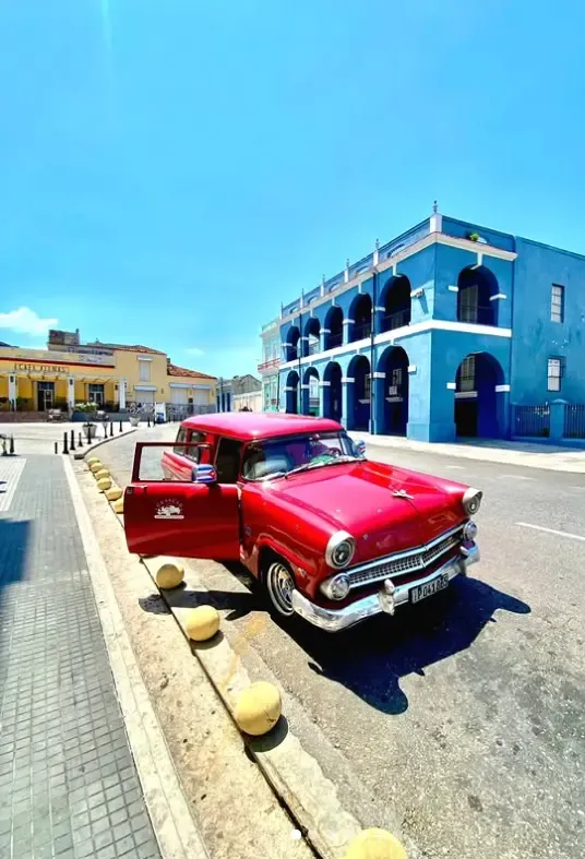 A red American car parked in front of a blue colonial building in Matanzas